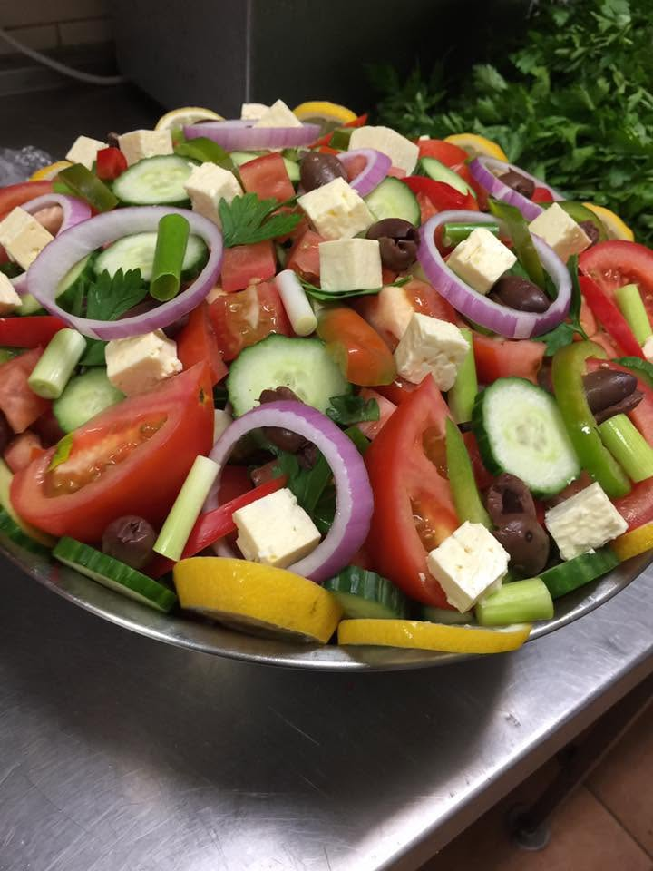 A steel bowl of Greek salad with feta, tomato, cucumber, red onion, olives and lemon