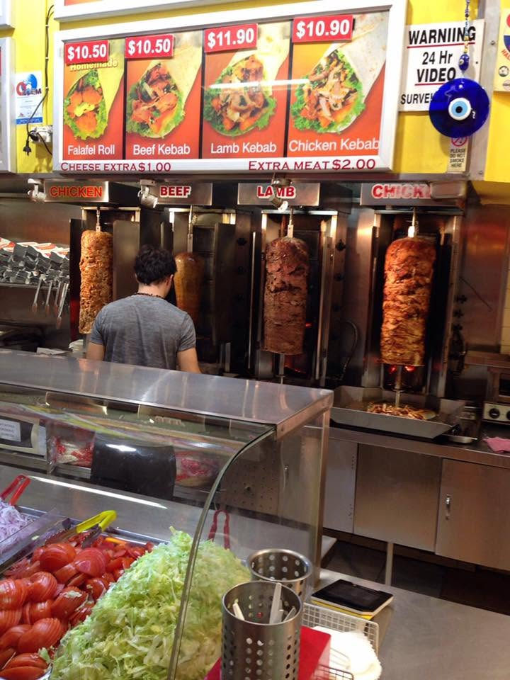 Four vertical rotisserie spits of chicken, beef and lamb meat turning on the grill at SHAH Kebabs