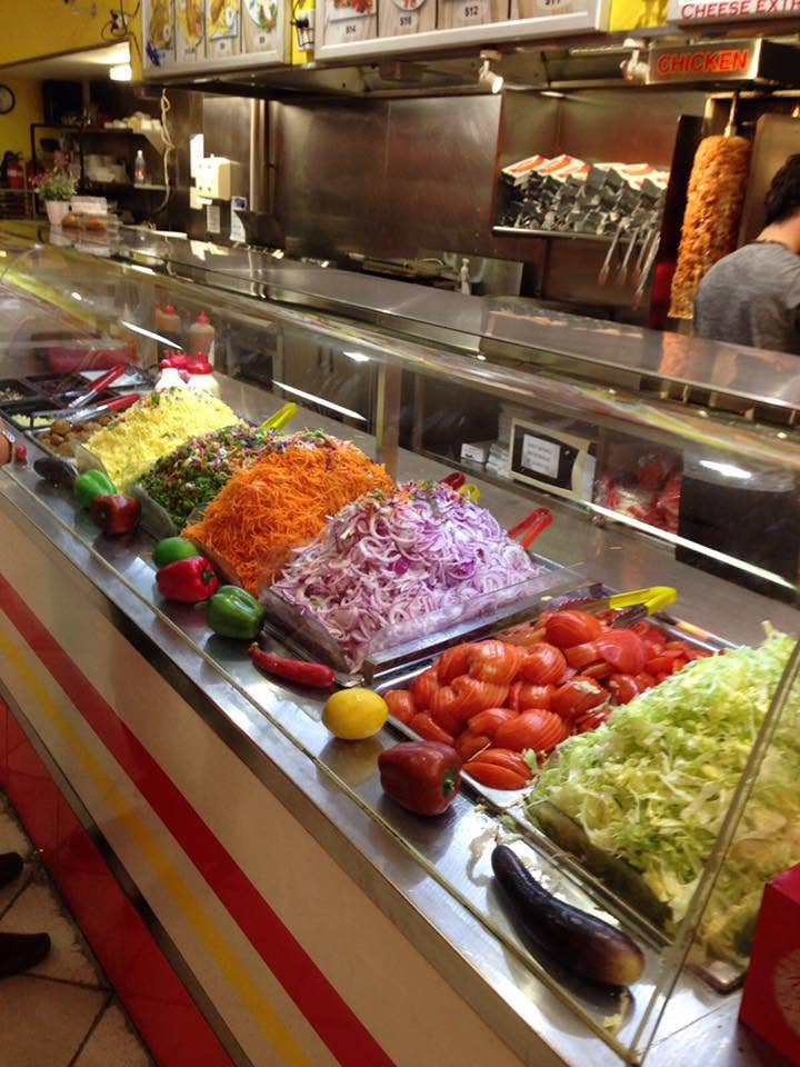 Looking down the SHAH Kebabs salad bar, with fresh vegetables along the rail and the grill behind